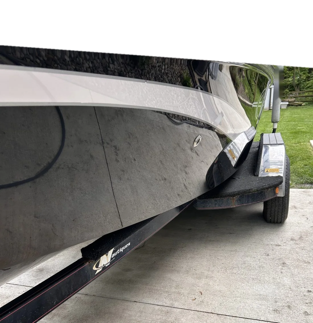 The hull of a black boat after a full gelcoat correction, with a white stripe and trees reflected in the finish